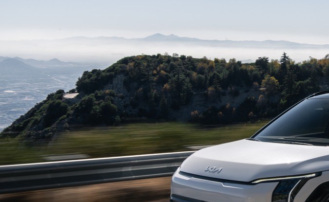 Kia EV3 2027 blanco circulando por una carretera de montaña con vista al mar