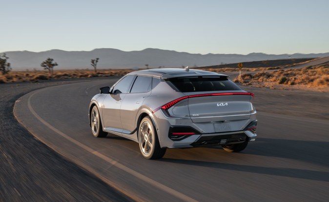 Parte trasera de un Kia EV6 gris tomando una curva en una carretera desértica.
