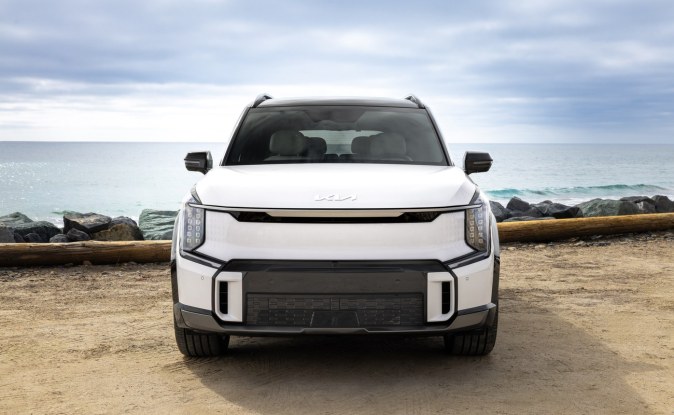 Kia EV9 blanco visto de frente, estacionado sobre arena frente al mar.