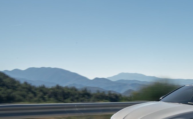 Kia K5 2027 gris circulando por una carretera de montaña con cielo despejado