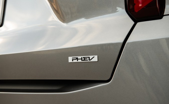 Primer plano del emblema PHEV en la compuerta trasera de una SUV Kia color gris claro.