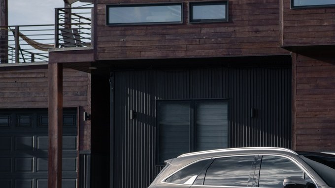 SUV Kia Sorento híbrida enchufable color arena estacionada frente a una casa moderna de madera oscura.
