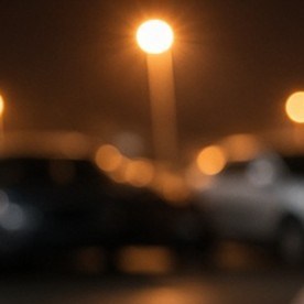 Mano con guante negro intenta abrir la puerta de un sedán gris en un estacionamiento iluminado de noche