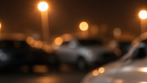 Mano con guante negro intenta abrir la puerta de un sedán gris en un estacionamiento iluminado de noche