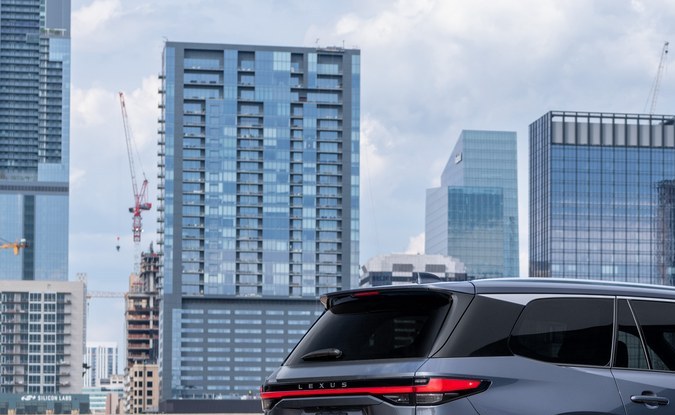 Vista trasera de un SUV Lexus TX gris estacionado en una azotea con edificios de la ciudad detrás.