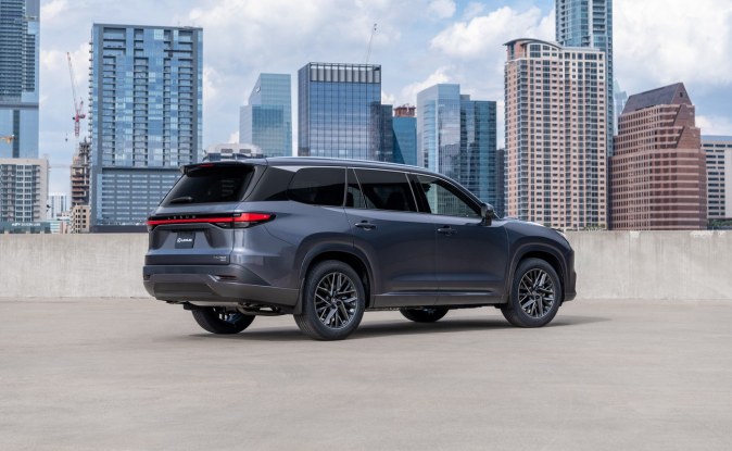 Vista trasera de un SUV Lexus TX gris estacionado en una azotea con edificios de la ciudad detrás.
