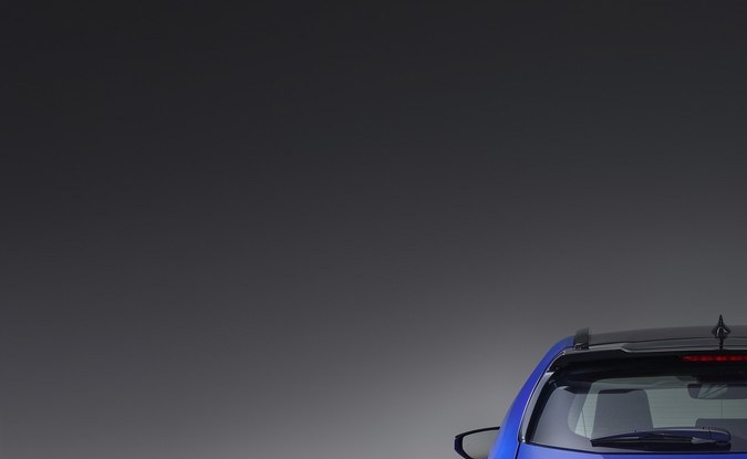 Vista trasera del Lexus UX 300h azul con su barra de luces traseras encendida, en un estudio gris.