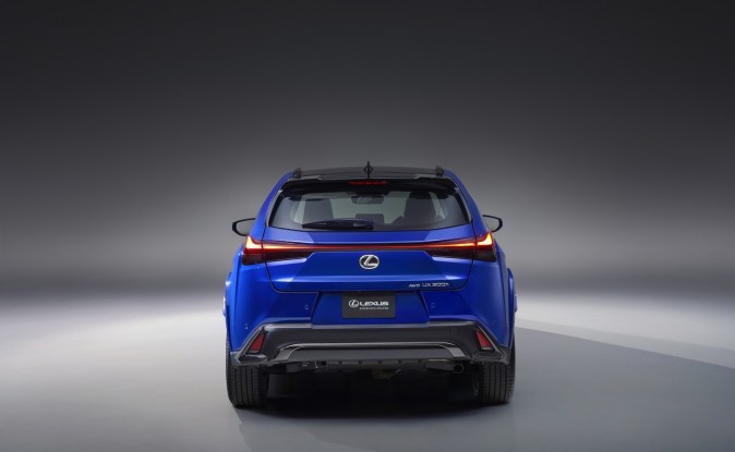 Vista trasera del Lexus UX 300h azul con su barra de luces traseras encendida, en un estudio gris.
