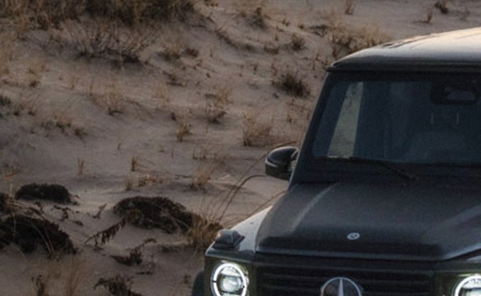 Mercedes-Benz Clase G negro de frente con los faros encendidos sobre un camino de tierra.