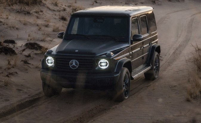 Mercedes-Benz Clase G negro de frente con los faros encendidos sobre un camino de tierra.