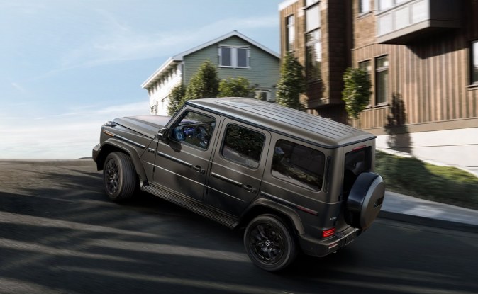 Mercedes-Benz Clase G gris oscuro subiendo una calle muy inclinada frente a casas modernas.