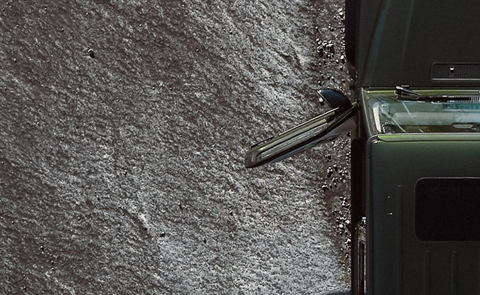 Vista aérea de un Mercedes-Benz Clase G oscuro avanzando sobre una superficie de roca gris.