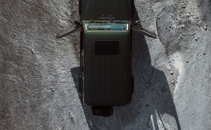Vista aérea de un Mercedes-Benz Clase G oscuro avanzando sobre una superficie de roca gris.