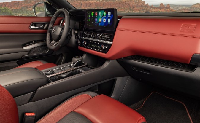 Interior de SUV con tapicería negra y borgoña, pantalla central y consola, visto desde el asiento del pasajero.