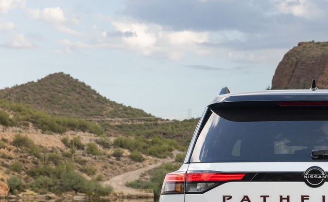 Parte trasera de una SUV Nissan Pathfinder blanca en un camino de tierra junto a un lago y montañas.