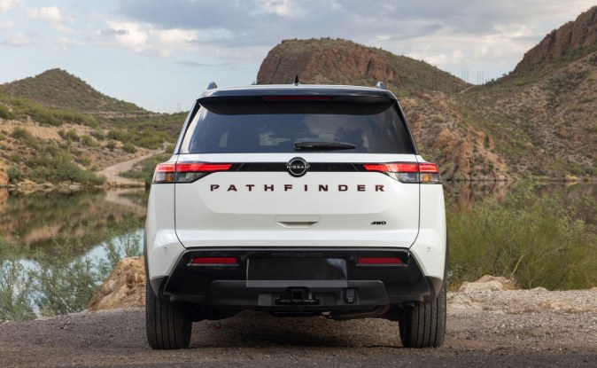 Parte trasera de una SUV Nissan Pathfinder blanca en un camino de tierra junto a un lago y montañas.