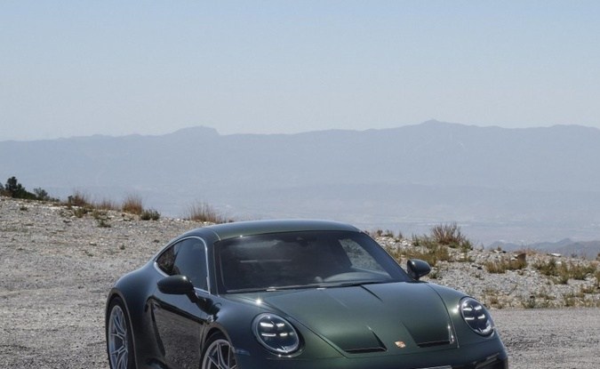 Dos Porsche 911 GT3, verde Touring y blanco con alerón, estacionados frente a montañas.