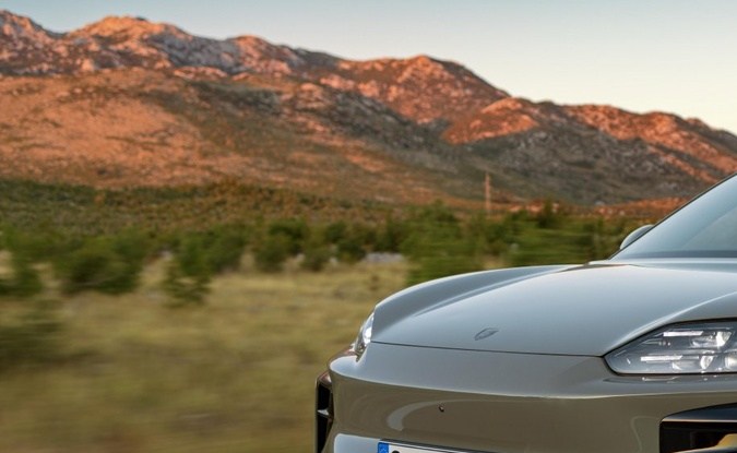 Porsche Macan verde con faros encendidos circulando al atardecer por un camino rural.