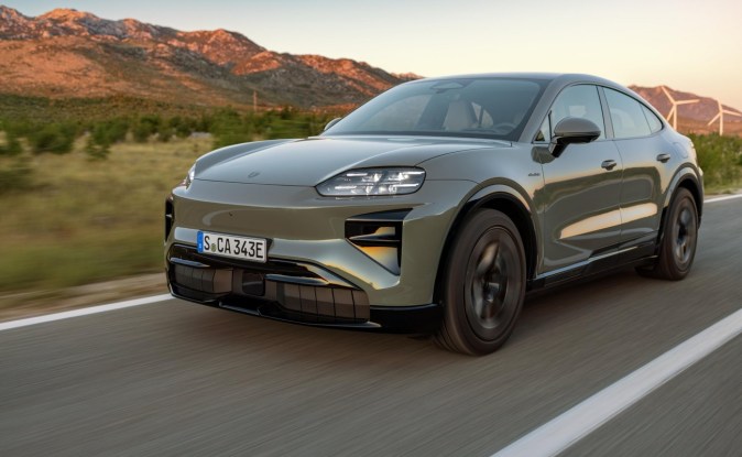 Porsche Macan verde con faros encendidos circulando al atardecer por un camino rural.