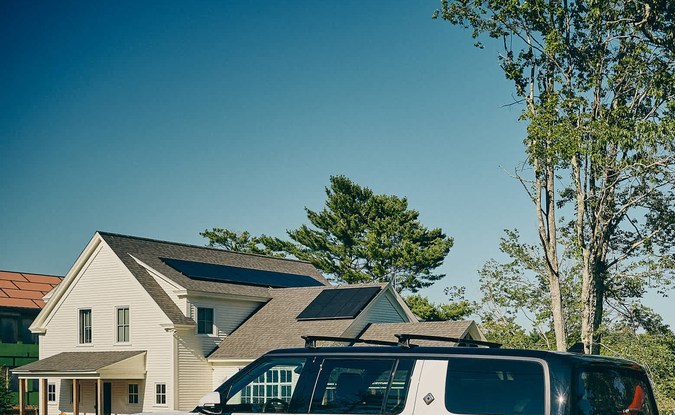 Rivian R1S blanco estacionado frente a una casa junto a un lago mientras una familia carga un kayak rojo