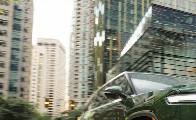 SUV Rivian R1S verde oscuro en una calle urbana rodeada de edificios altos.