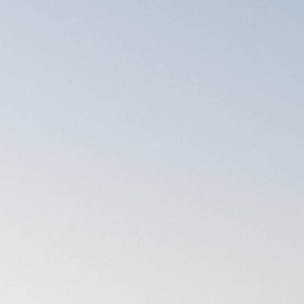 SUV eléctrico Rivian R2 azul circulando por una carretera de montaña con curvas al atardecer.