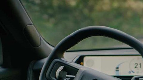Interior de un Rivian R2 en marcha, con el conductor sin manos en el volante y la pantalla encendida.