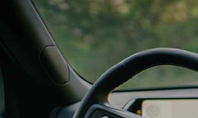 Interior de un Rivian R2 en marcha, con el conductor sin manos en el volante y la pantalla encendida.