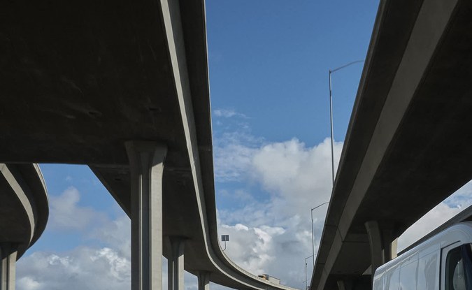 Van eléctrica de reparto Rivian blanca circulando bajo un paso elevado de autopista.