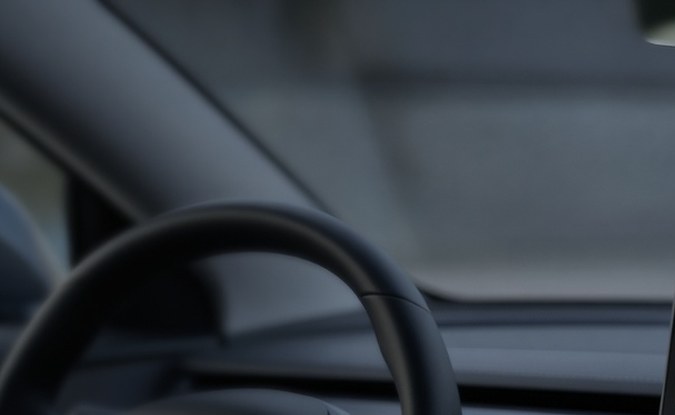 Interior de un auto eléctrico con volante, pantalla central con un mapa abstracto y una cámara bajo el espejo retrovisor.