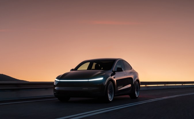 SUV eléctrico de Tesla oscuro con faros encendidos circulando por una carretera al atardecer