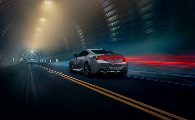 Toyota GR86 plateado circula de noche por un túnel iluminado.