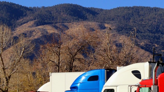 Fila de tractocamiones de colores estacionados en un área de descanso de una carretera de California, con montañas al fondo