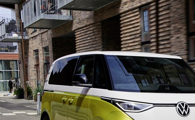 Volkswagen ID. Buzz bitono amarillo Pomelo y blanco circulando por una calle urbana junto a un edificio de ladrillo