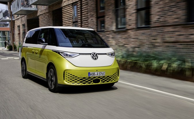 Volkswagen ID. Buzz bitono amarillo Pomelo y blanco circulando por una calle urbana junto a un edificio de ladrillo
