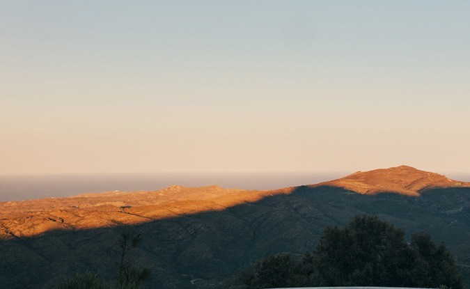 Volvo EX60 plateado circulando por una carretera de montaña al atardecer con un valle al fondo
